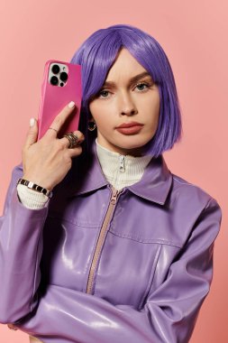 Canlı stil sahibi bir kadın pembe bir fona telefon tutarken mor saçlarını gösteriyor..