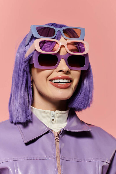 A vibrant woman showcases her stylish look with multiple pairs of sunglasses on a pink backdrop.