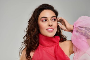 Kadın, kendine güvenerek gülümserken yumuşak renklerde şık bir kıyafet sergiliyor..