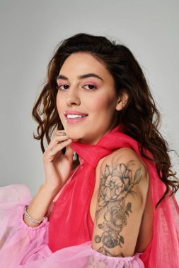Genç bir kadın stüdyoda canlı bir kıyafet giyerken gülümseyerek dövmelerini sergiliyor..