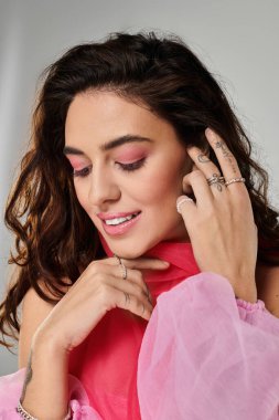 Zarif genç bir kadın, pembe giysiler içinde, doğal güzelliğini göstererek hafifçe gülümsüyor..