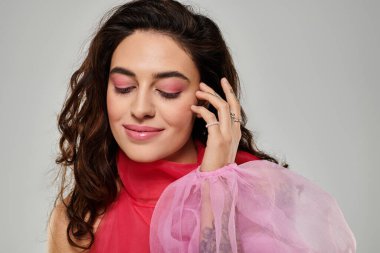 Pembe elbiseli genç bir kadın zarif bir şekilde yüzüne dokunuyor..