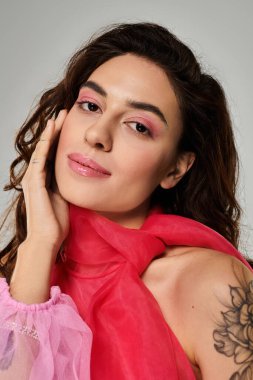 Dalgalı saçlı ve makyajlı kadın canlı pembe bir eşarp takarken güzellik sergiliyor.