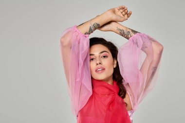 Pembe ve kırmızı elbiseli kadın kendine güvenerek poz veriyor, canlı moda ve dövme sergiliyor..