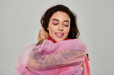 Genç ve güzel bir kadın pembe bir kumaşı kucaklarken canlı makyajını sergiliyor..