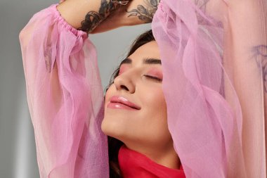 Anlamlı dövmeleri olan genç bir kadın pembe elbiseleriyle huzurlu bir anı kucaklıyor..