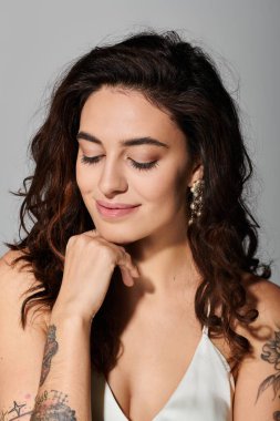 Kıvırcık saçlı ve dövmeli bir kadın fotoğraf çekilirken nazikçe gülümserken zarafet sergiler.