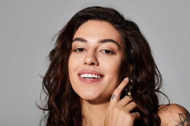 Siyah saçlı genç bir kadın gülümsüyor ve yüzlerine küpe takarken dokunuyor..