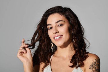 Güzel genç bir kadın gülümser ve saçlarına dokunur, kendine güveni ve cazibesi yayılır..