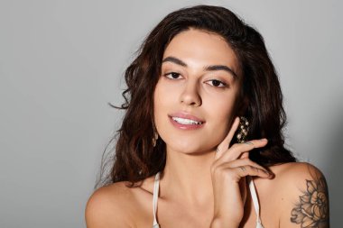 Genç ve güzel bir kadın zarif görünüşünü ve dövmesini gösterirken usulca gülümsüyor..