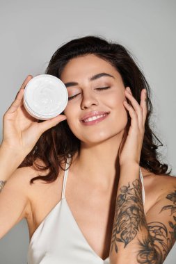 Güzel genç bir kadın gülümserken ve güzellik rutininin tadını çıkarırken elinde bir cilt ürünü tutuyor..