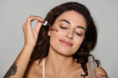 Kadın yüzüne serumu nazikçe sürerken gülümsüyor. Güzelliğini ve cildini gösteriyor..