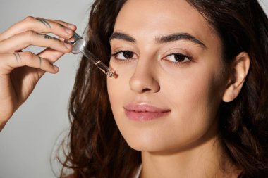 Güzel genç bir kadın yüzüne serum serumu serpmek için bir damlatıcı kullanıyor..