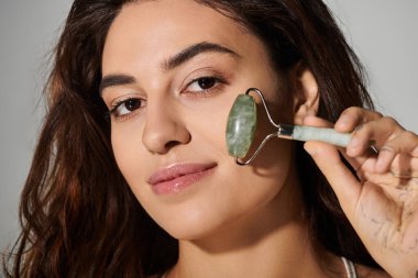 Genç bir kadın, cilt bakımına odaklanmış sakin bir şekilde yüzüne yeşim taşı takıyor..