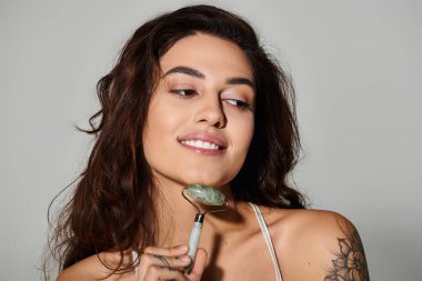 Kadın, yumuşak renklere sahip iyi ışıklandırılmış bir ortamda yeşim taşıyla cilt bakımını seviyor..