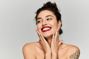 Işıl ışıl gülümseyen genç bir kadın basit bir stüdyo arka planında sevinçle poz veriyor..