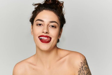 Kadın neşeyle gülümser, kendine güvenen kişiliği ve kalın kırmızı dudaklarıyla.