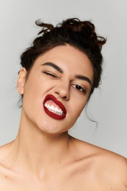 Beautiful woman with striking red lips making a playful face in a simple studio backdrop clipart