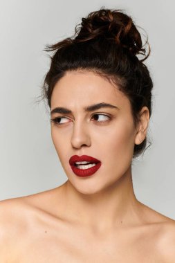 Cesur kırmızı dudakları olan genç bir kadın sade bir arkaplanda büyüleyici bir ifade sergiliyor..