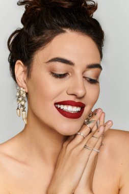 Young woman displays her radiant smile and fashionable jewelry against a neutral background. clipart