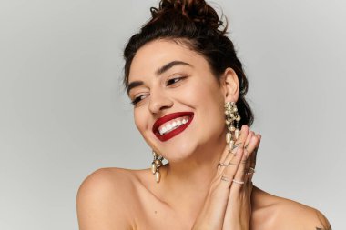 Genç bir kadın neşeyle gülümser, zarif küpeler ve yüzükler takar..