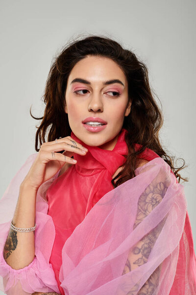 Young woman with striking makeup and vibrant clothing poses confidently against a plain background.