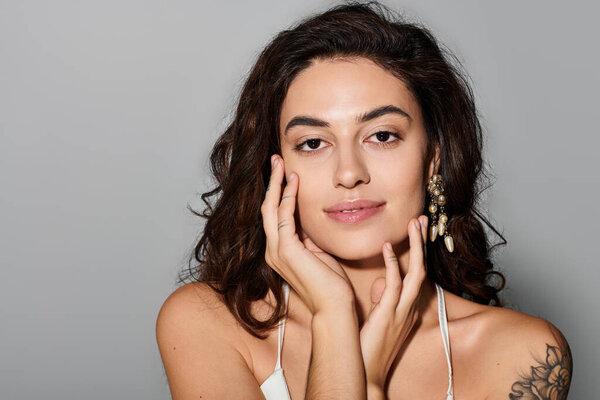 A young woman smiles softly, touching her face and revealing her natural beauty indoors.