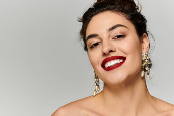 A young beautiful woman showcases a radiant smile while wearing stunning earrings and lipstick.