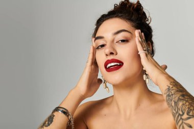 Güzel, genç bir kadın, elleri yüzü üzerinde güven içinde poz veriyor, ifadesini sergiliyor..