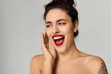 Siyah saçlı ve kırmızı rujlu genç bir kadın stüdyoda neşe ve heyecan ifade ediyor..