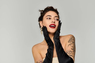 Woman with tattoos poses with black gloves and bold lipstick, showcasing elegance and charm. clipart