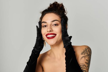 Kendine güvenen bir gülümsemesi olan genç bir kadın siyah eldivenlerle poz veriyor, büyüleyici ve tarz sahibi..