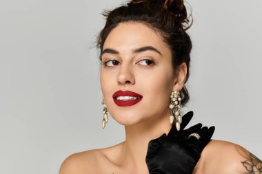 Young woman with dark hair and red lips wears classy earrings and gloves while posing stylishly. clipart