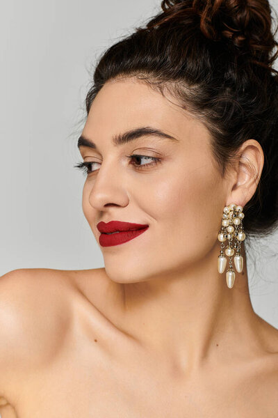 Молодая женщина уверенно улыбается, надевая серьги и ярко-красную помаду..