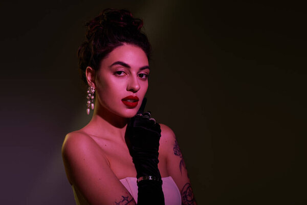 Женщина демонстрирует изысканность с перчатками и яркими аксессуарами в мягком свете.