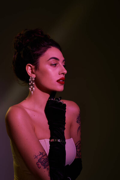 Элегантная женщина с темными волосами и смелым макияжем позирует в черных перчатках и сережках.