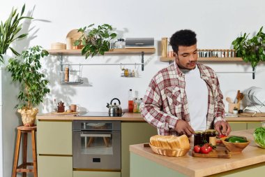 Ekose gömlekli genç adam bitkilerle dolu minimalist bir mutfakta sebze doğruyor..