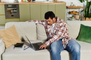 Young man focused on laptop tasks in a stylish, cozy living space with green accents. clipart