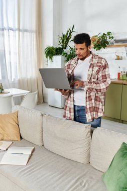 Yakışıklı genç adam şık bir oturma odasında dikilirken dizüstü bilgisayarda yazı yazıyor.