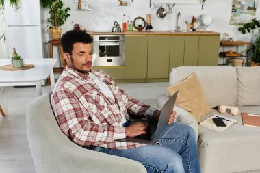 Yakışıklı genç adam şık bir ev ortamında dizüstü bilgisayarına odaklanmış..