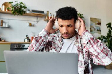 Gündelik kıyafetli genç adam, dizüstü bilgisayarda kulaklıkla şık bir yerde çalışıyor..