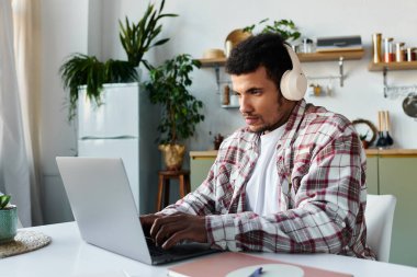 Kulaklık takan yakışıklı genç adam rahat ofisinde laptopuna dikkatle odaklanıyor..