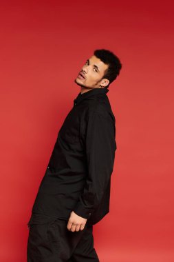 Yakışıklı genç adam parlak kırmızı bir arkaplan önünde güvenle dururken başını eğer.