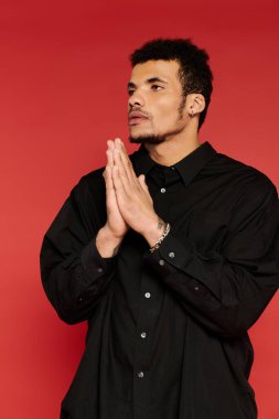 Siyah gömlekli adam ellerini birbirine bastırarak düşünceli bir poz veriyor..