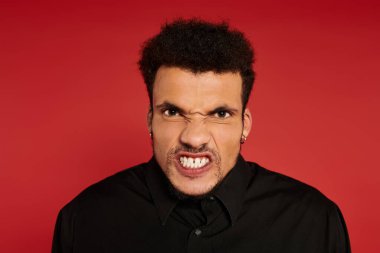 A young handsome man with curly hair displays a fierce expression against a red backdrop. clipart