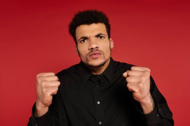 Genç bir adam kendine güvenen bir poz veriyor. Yumruklarını sıkmış ve ciddi bir ifade takınıyor..