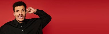 Handsome young man with curly hair shows surprise against a bold red backdrop wearing a black shirt clipart