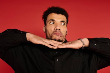 Young man displays a fun expression, hands raised near his chin, set against a vibrant red backdrop. clipart