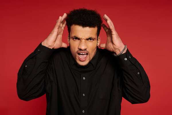 Молодой красивый мужчина показывает сильные эмоции, руки на голове, создавая поразительное воздействие.