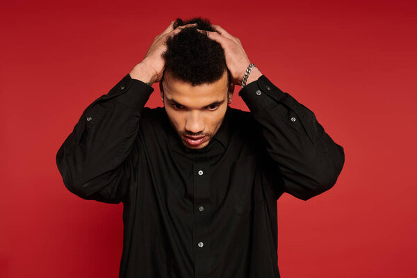A young man stands confidently, styling his hair while wearing a black shirt.